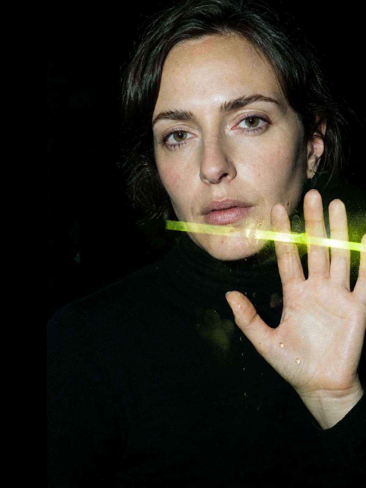 A self-possessed adult looking through an acrylic surface with one hand raised toward it.